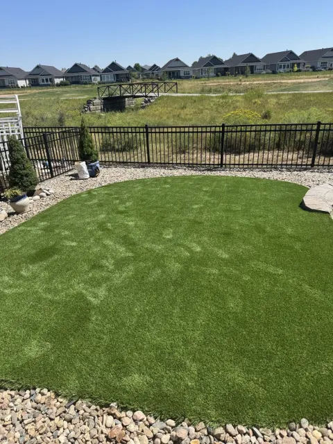 Groomed artificial lawn in a fenced yard with a rock border