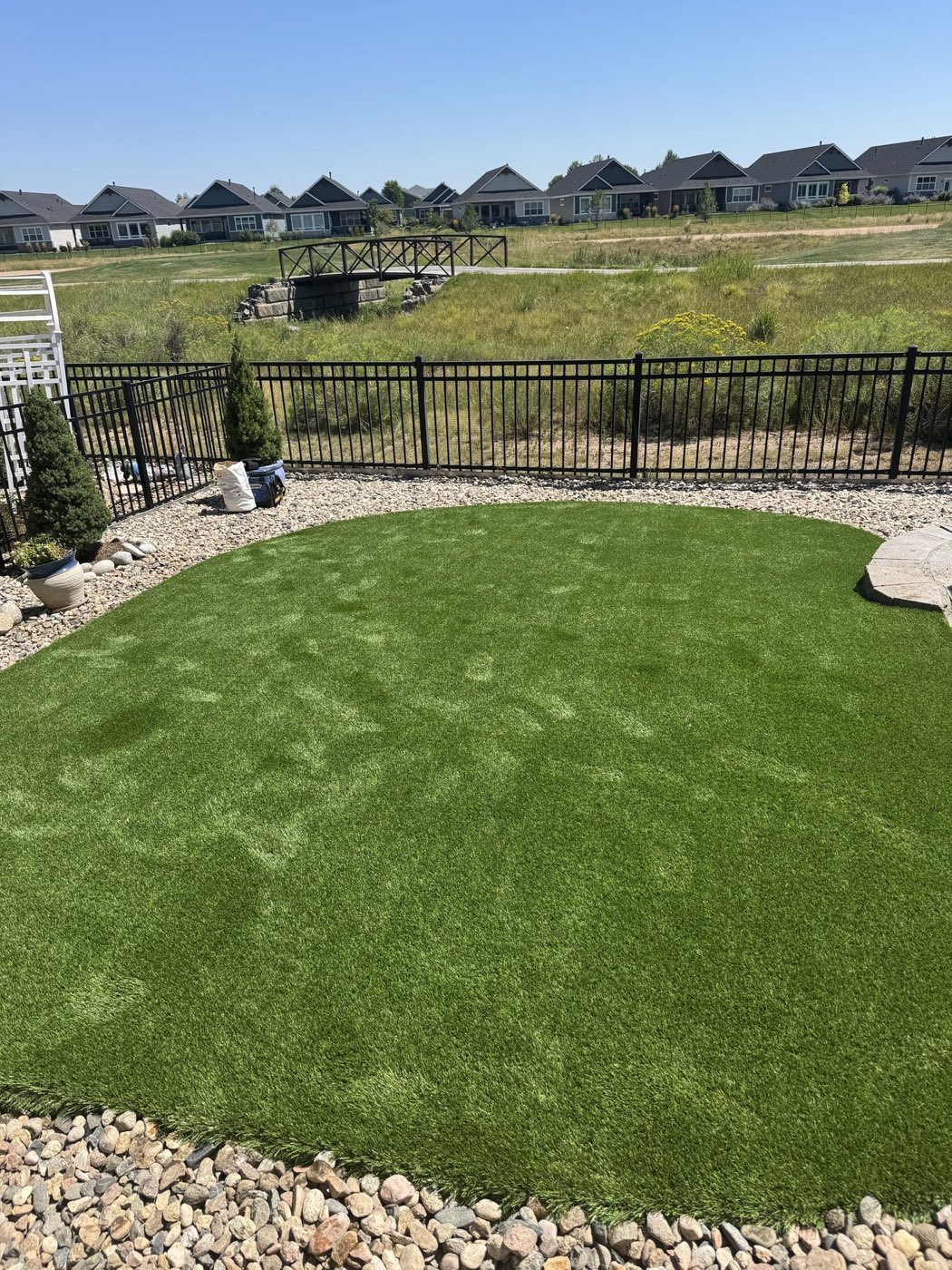 Groomed artificial lawn in a fenced yard with a rock border
