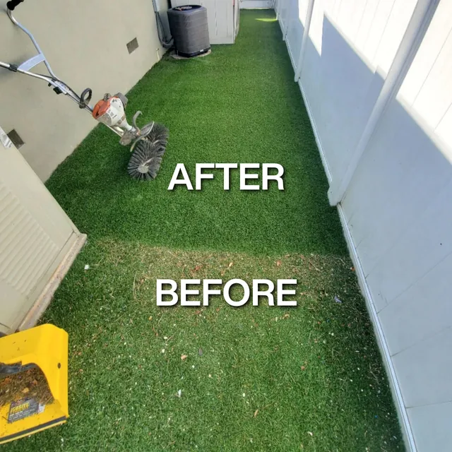 Narrow side-yard artificial turf half cleaned, with a power brush resting on the finished section