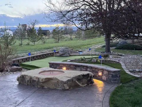 Backyard putting green beside a stone wall and fire pit