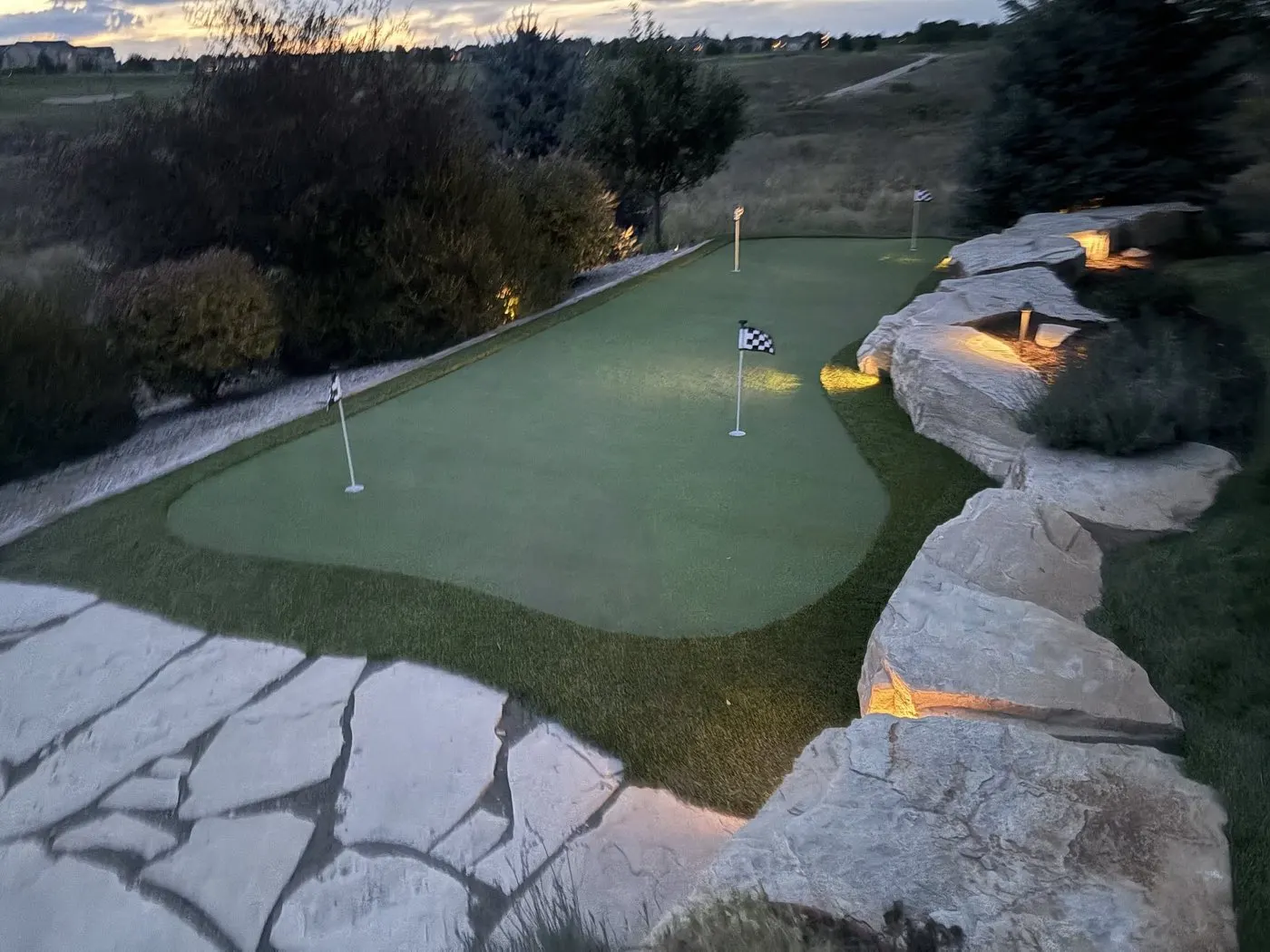 Backyard putting green with landscape lighting at dusk