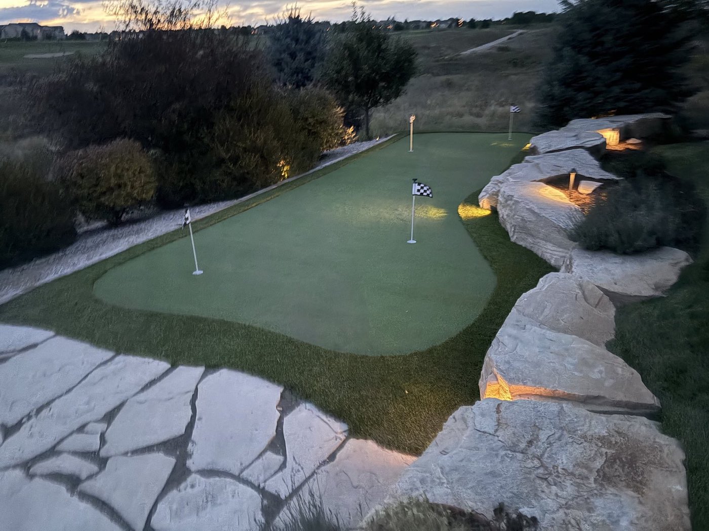 Backyard putting green with landscape lighting at dusk